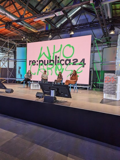 Vier Frauen sitzen auf einer großen Bühne. Hinter ihnen auf der Leinwand steht Re:publica 24 und in neon grün wie ein Graffiti who cares. 