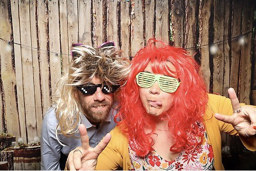 Zwei Menschen mit bunten Perücken und Sonnenbrillen in einer Fotobox.