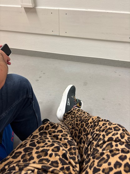 grauer Betonfußboden, ein Bein in Jeans. Zwei Füße in schwarzen Turnschuhen.