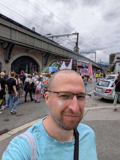 Ich, Person Mitte Dreißig, mit einem Glitzerherz auf der Wange vor dem Demozug mit Prideflaggen. Demozug von hinten, damit keine Gesichter erkennbar sind. 