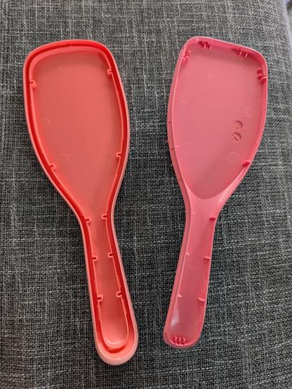 Lachsarbene Haarbürste aus Plastik in zwei Teile zerlegt. Die Innenseite der Bürste hat zehn Punkte, an denen die Teile ineinander verhaken. Vier am Bürstenkopf und sechs am Griff. 