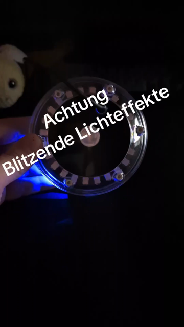 Zwei Hände halten ein durchsichtiges, runden Plastikteil. Drinnen leuchten ringförmig LEDs auf. Immer wenn gesprochen wird. Bei tiefen Tönen gelblich, bei hohen blau und grün. Je lauter, desto mehr LEDs leuchten von unten links und rechts nach oben. 