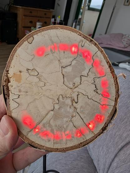 Eine etwa 10 Zentimeter große Holzscheibe, durch die in einem Dreiviertelkreis Licht durchscheint. 