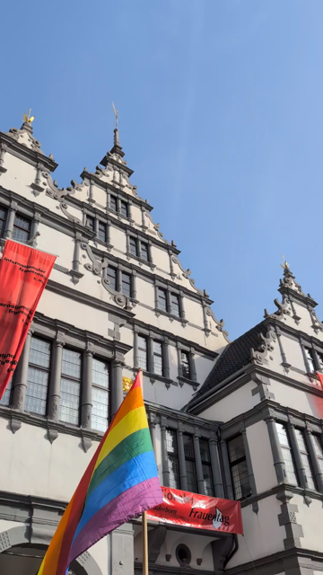 Das Rathaus von Paderborn mit roten Flaggen zum Weltfrauentag. Davor weht eine Regenbogenflagge. Die Menschen der Demo sind auf dem Video nicht zu sehen, sondern nur zu hören. Sie rufen: “Alerta, Alerta Queerfeminista”.