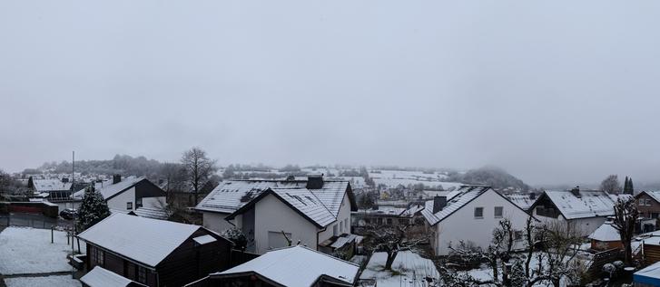 Schneebedeckte Hausdächer und Nebel darüber.