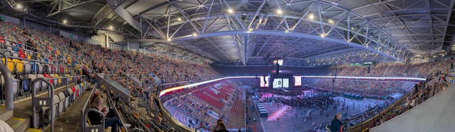 Panoramaaufnahme der Merkurarena in Düsseldorf. Aufgenommen von einem Sitzplatz im oberen Rang. Am anderen Ende der Arena ist eine Bühne aufgebaut, mit dem Robbie Williams Logo. Die Ränge sind fast leer, Stehplätze am Boden zu etwa einem Drittel gefüllt.