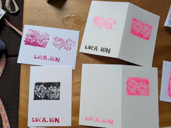 Vier bedruckte Karten auf einem Tisch. Die Motive sehen ein bisschen aus wie Schaltkreise in einer Unendlichkeitsschlaufe. Sie sind in pink und schwarz. Jeweils unten oder auf der Rückseite ist luca.run gedruckt